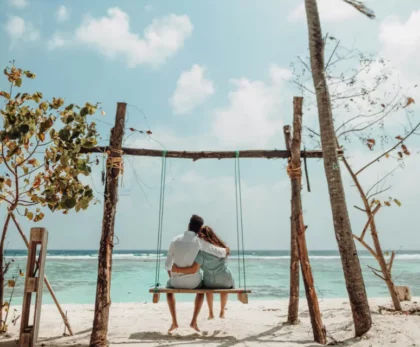 couple romantique en voyage de noces au Maroc. Le couple est en train de s'embrasser sur une plage Marocaine de sable blanc, avec des eaux turquoise et des palmiers en arrière-plan.